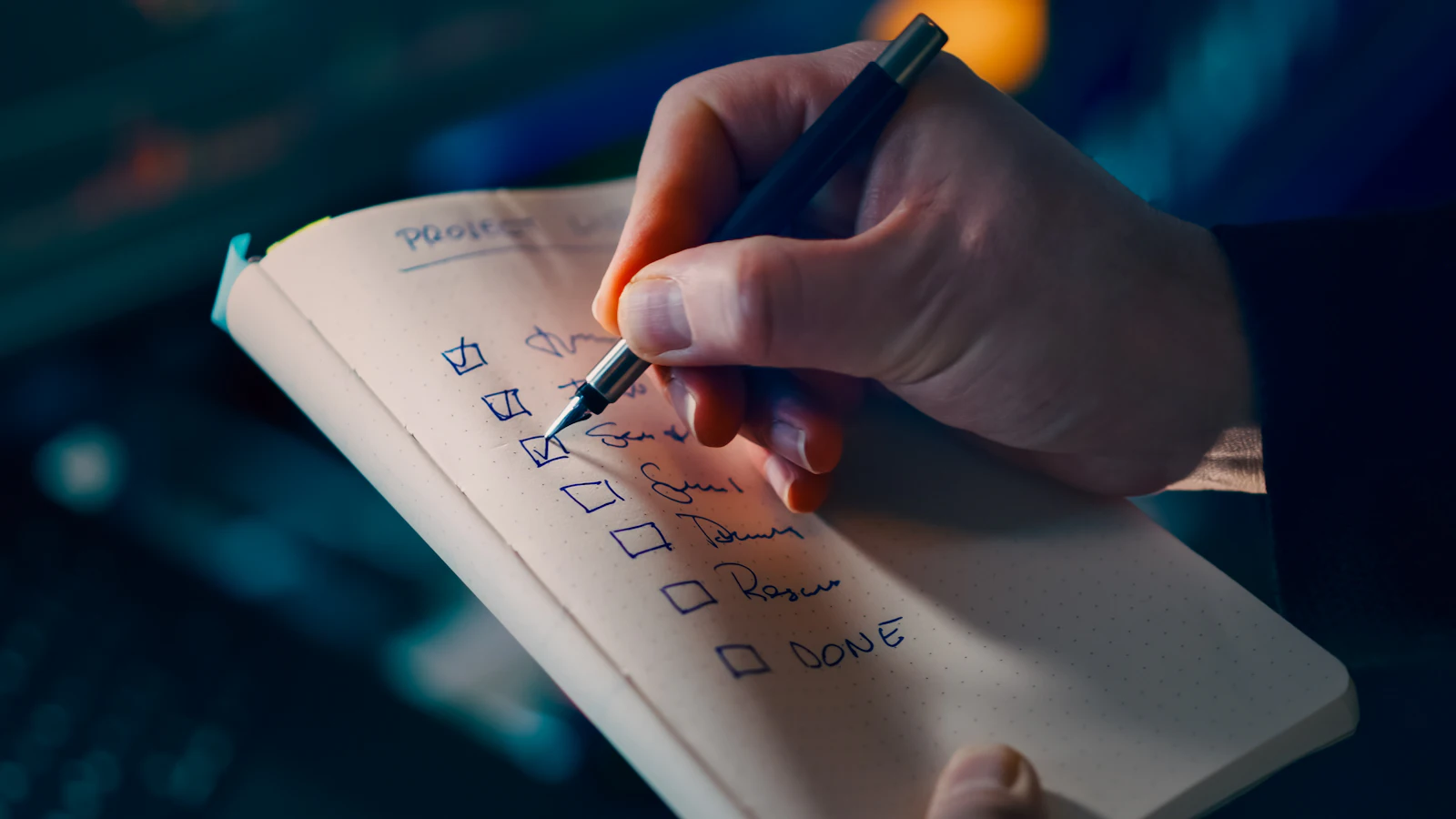 Founder crossing items off a handwritten task list next to a laptop and a cup of coffee