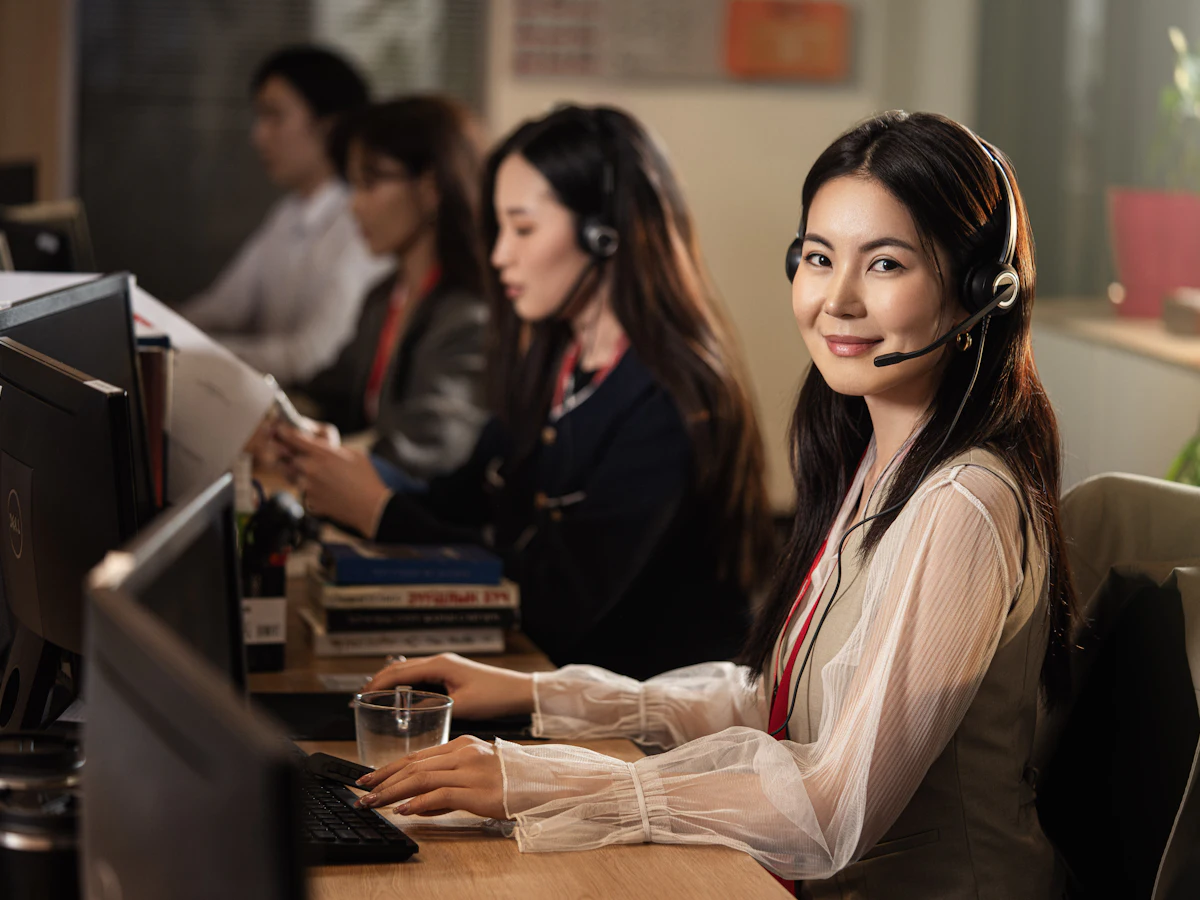 Filipina virtual assistant wearing a headset, working at a modern desk with two monitors in soft natural light