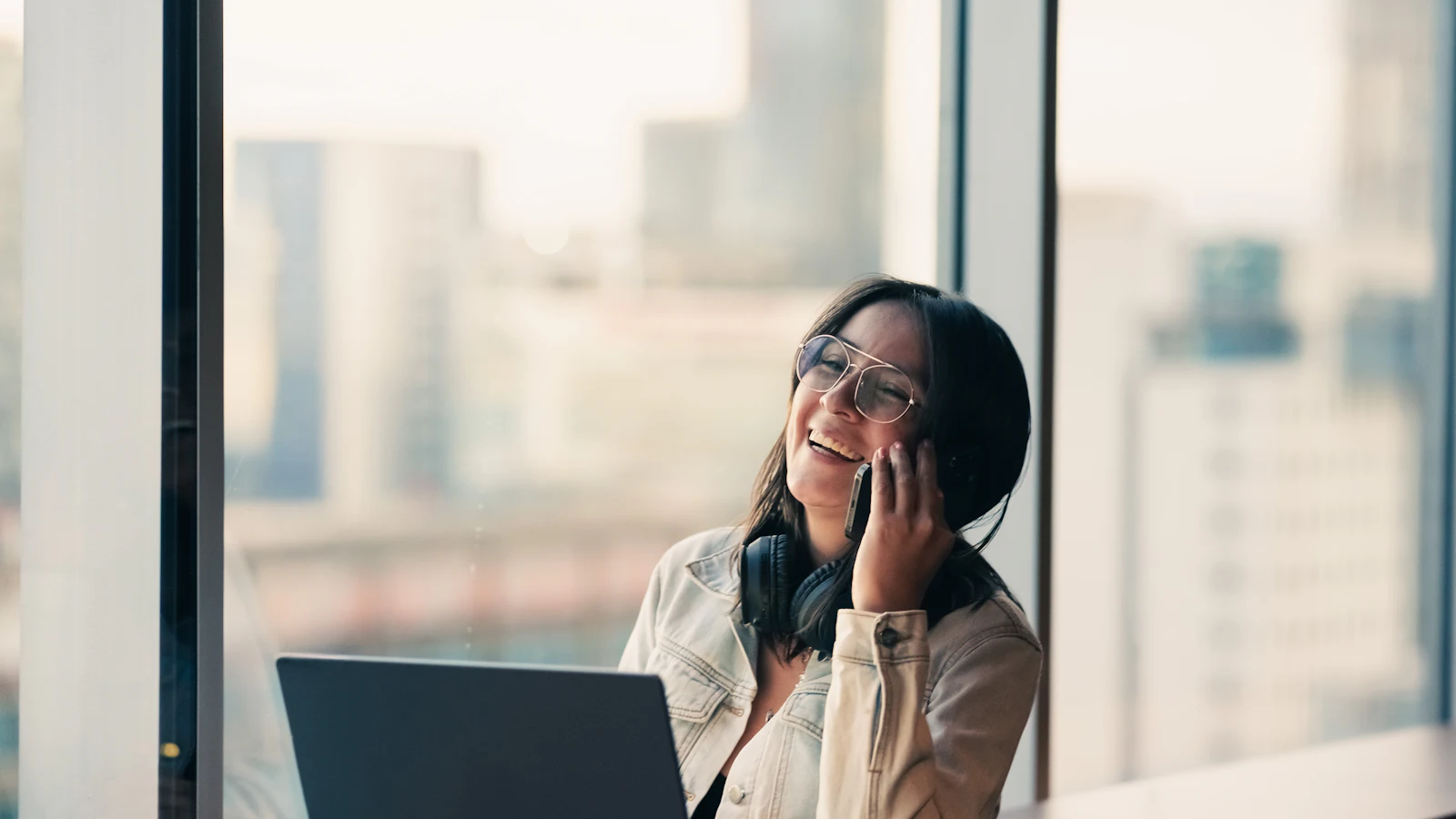 Smiling Asian virtual assistant on a call with a client, laptop open, city view behind her